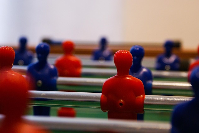 A close-up of a foosball table with red and blue plastic players lined up in similar positions. The image represents the concept of copying competitors in branding, illustrating a lack of uniqueness and differentiation.